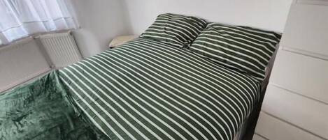 A bed with a striped bedspread and pillows, a bedside table, and a radiator.