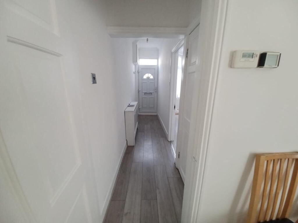 Ein schmaler Flur mit einer Tür am Ende, einem Thermostat an der Wand und einem Sessel in der Ecke.