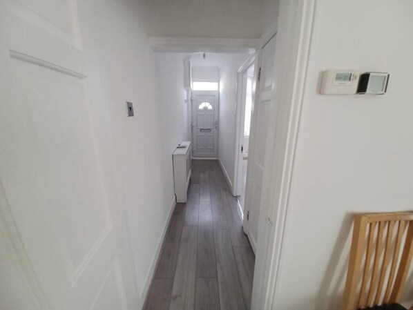 A narrow hallway with a door at the end, a thermostat on the wall, and a chair in the corner. - The Maple (Grays)