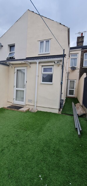 A residential building with a sloped roof, a front door, and a small front yard with artificial grass.