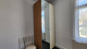 A room with a single chair, a mirror, a radiator, and a window.