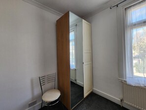 A room with a single chair, a mirror, a radiator, and a window.