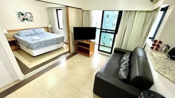 Quarto de hotel com cama, televisão, sofá e janela com cortinas.