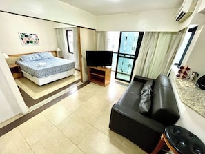 Quarto de hotel com cama, televisão, sofá e janela com cortinas.