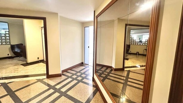 Un pasillo con piso de diseño geométrico, un espejo grande que refleja la habitación, y una puerta que da a otro espacio.