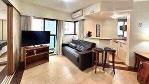 Sala de estar con televisor de pantalla plana, sofá, mesa de centro y área de cocina con mostrador y armarios.