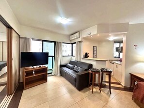 Ein Wohnzimmer mit Flachbildfernseher, einer Couch, einem Couchtisch und einer Küchenzeile mit Arbeitsplatte und Schränken.