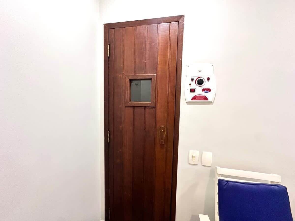A wooden door with a small window, a white wall with a thermostat, and a blue chair.
