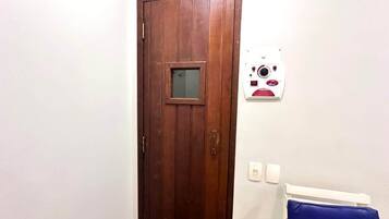 A wooden door with a small window, a white wall with a thermostat, and a blue chair.