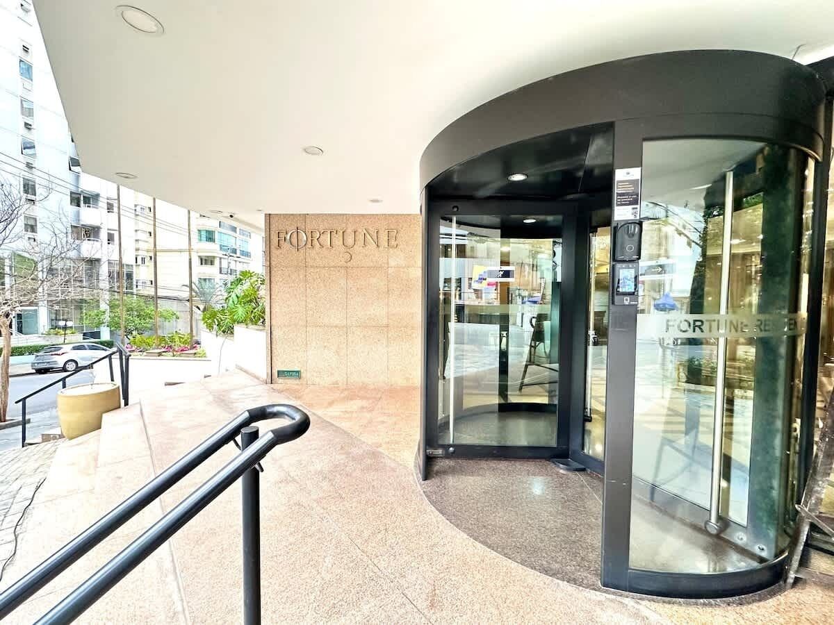 A modern building entrance with a curved glass door, a visible 'FORTUNE' sign, and a metal handrail.