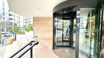 A modern building entrance with a curved glass door, a visible 'FORTUNE' sign, and a metal handrail.
