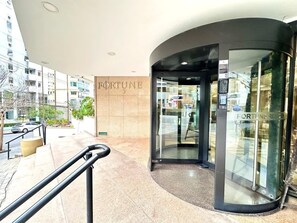 A modern building entrance with a curved glass door, a visible 'FORTUNE' sign, and a metal handrail. - Fortune Residence (São Paulo)