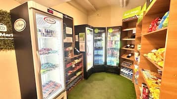 Um espaço pequeno e fechado com máquinas de venda automática e prateleiras repletas de lanches e bebidas.