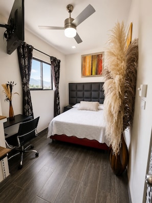 A modern bedroom with a bed, a desk, a chair, a ceiling fan, and a window with curtains. - Prado Centro #11 Luxury Suite - Jacuzzi & Wi-Fi (Medellín)