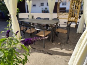 Ein Essbereich im Freien mit Tisch und Stühlen, umgeben von weißen Vorhängen und einer Schaukel.