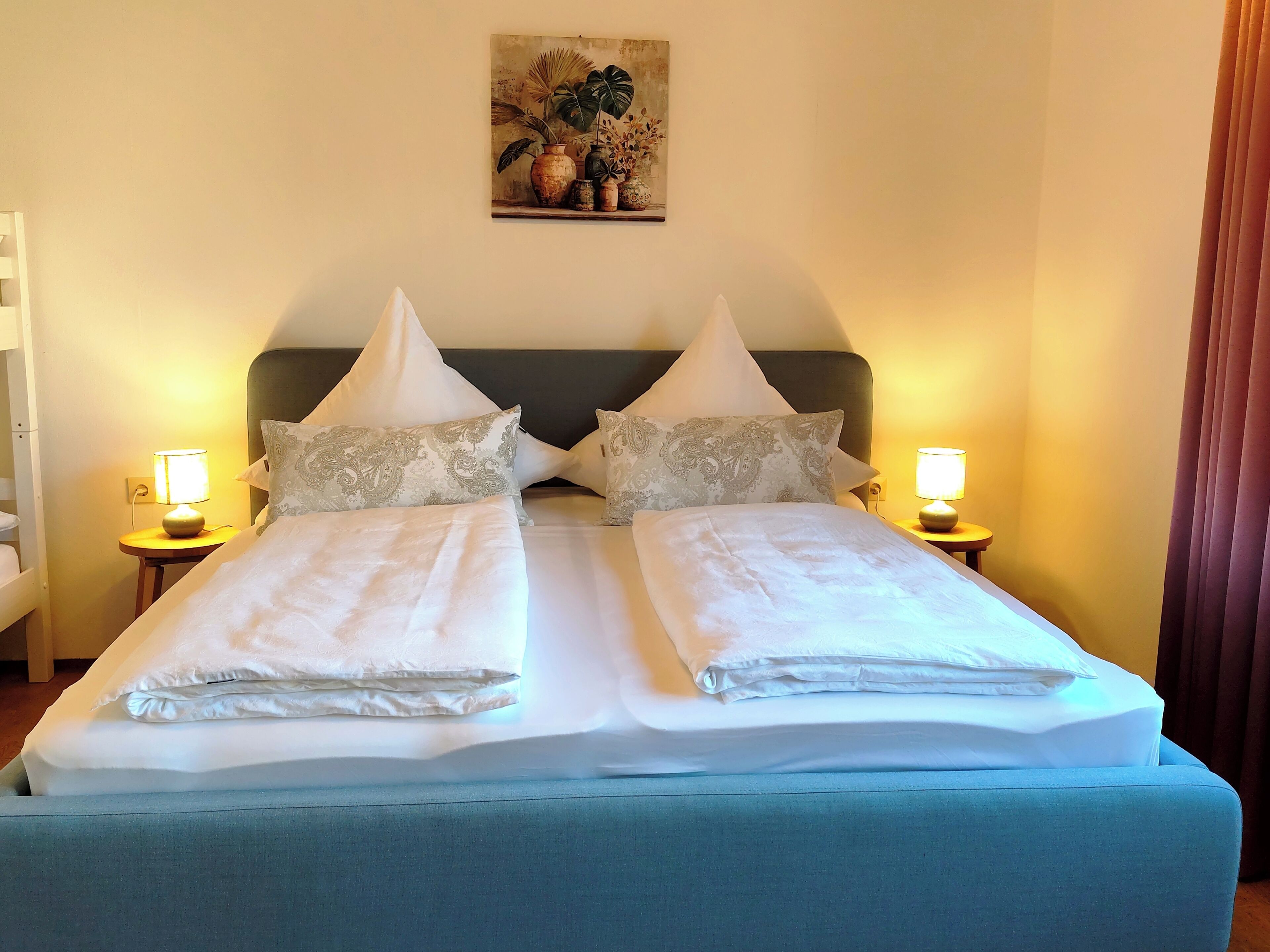 A double bed with two nightstands, each with a lamp, in a room with a painting on the wall.