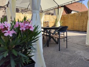 Eine Terrasse im Freien mit Tisch und Stühlen, einem Holzzaun und einem Blumentopf mit rosa Blüten.