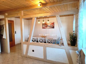 Ein Zimmer mit einem sechseckig gefliesten Boden, Holzbalken, einem Esstisch mit Stühlen und einem Bild an der Wand.