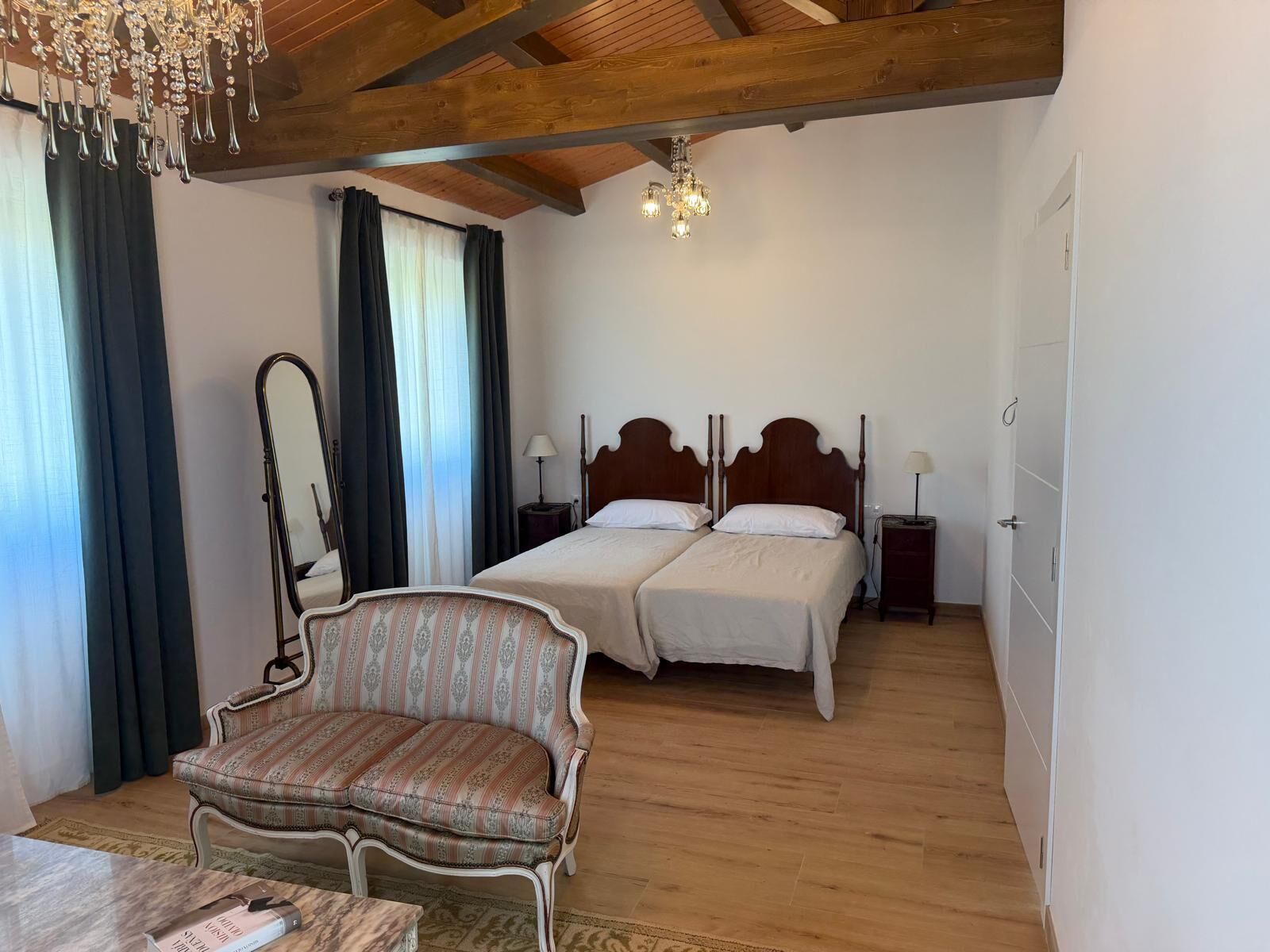 Quarto com duas camas, uma cadeira, um espelho e um lustre.