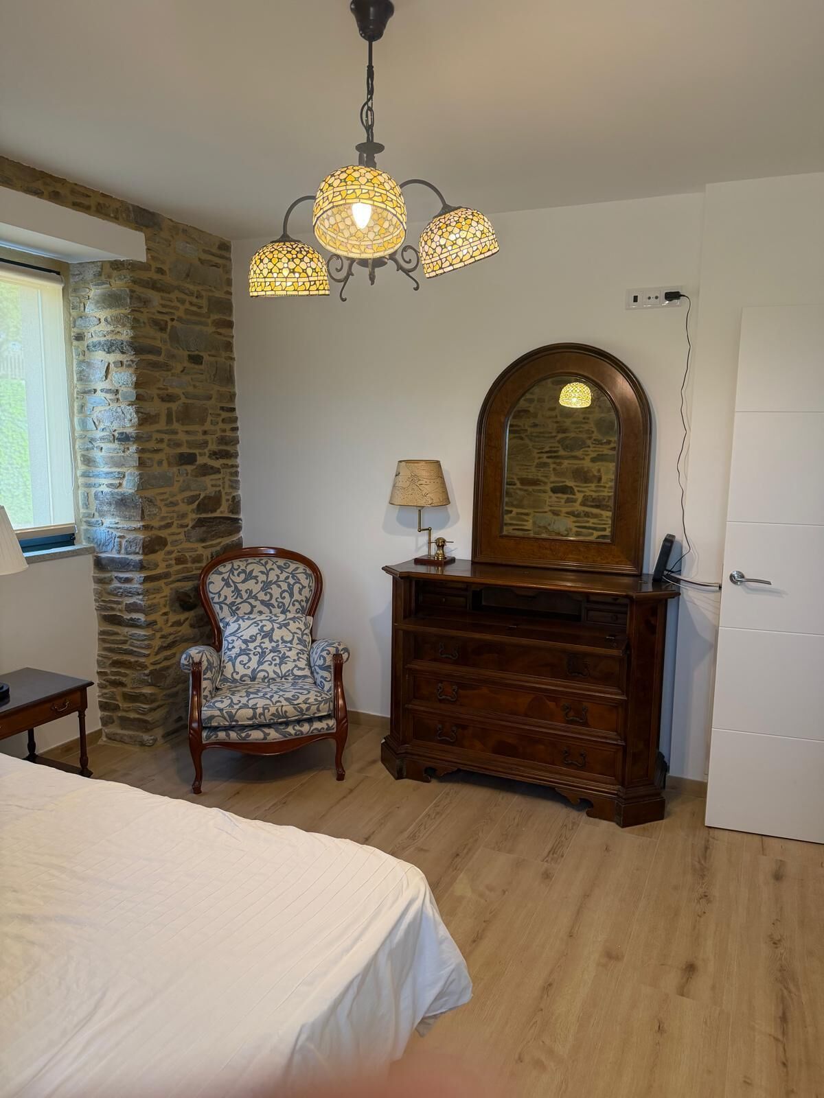 Een slaapkamer met een bed, een stoel, een dressoir, een spiegel en een kroonluchter.