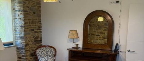 Un dormitorio con cama, una silla, tocador, espejo y candelabro.