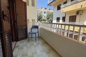 A balcony with a wooden gate, a chair, and a view of neighboring buildings. - La Maison Mikonos - superior apartment near the sea (Paola)