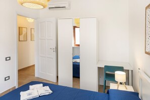A hotel room with a bed, a desk, a chair, and a lamp. There is a door leading to another room. - La Maison Mikonos - superior apartment near the sea (Paola)