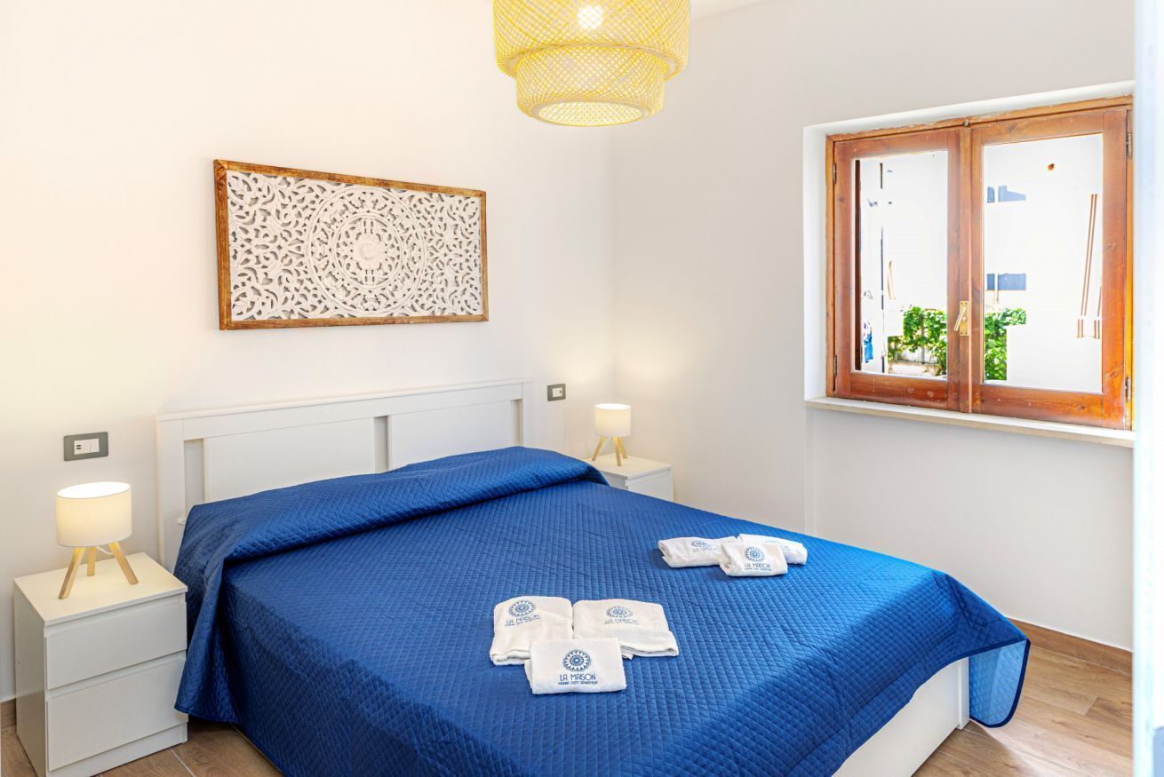 Una camera da letto con un letto, due comodini, un pannello decorativo a parete, una finestra con vista e una lampada a sospensione.