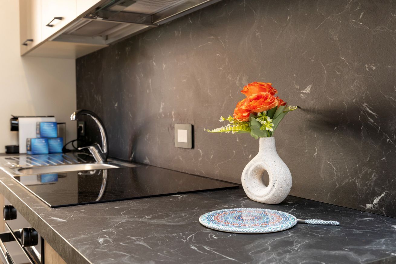 Un piano di lavoro da cucina con un moderno fornello, un vaso bianco con fiori e un piatto decorativo.