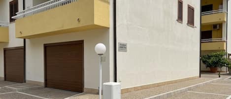 A building with a yellow balcony, a white light pole, and a closed brown door.