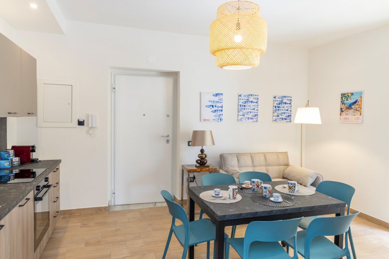 A modern dining area with a table set for two, blue chairs, a hanging light fixture, and wall art.