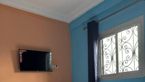 A bedroom with a bed, a TV mounted on the wall, and a window with decorative iron bars. - Elegant 1 BDR Apt | in Comfort & Style (Yaoundé)