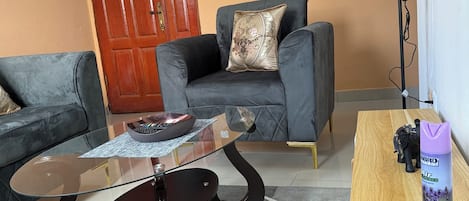 A living room with a sofa, a glass coffee table, a wooden side table, and a decorative lamp.