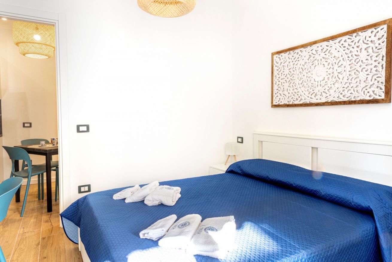 A hotel room with a bed, a table, chairs, a wall-mounted decorative piece, and a hanging light fixture.