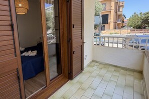 Ein Balkon mit einer Holztür, die zu einem Zimmer mit einem Bett und einer Pendelleuchte führt.