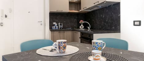 A compact kitchen with a dark countertop, a white door, and a dining table with two chairs.