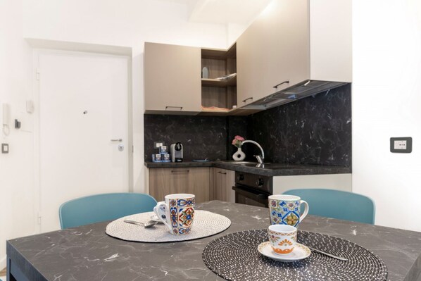 A compact kitchen with a dark countertop, a white door, and a dining table with two chairs.