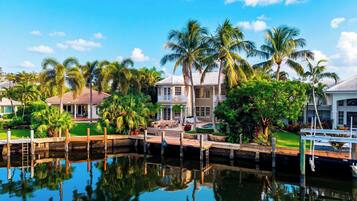 A waterfront property with a pool, a dock, and a well-maintained garden with palm trees.