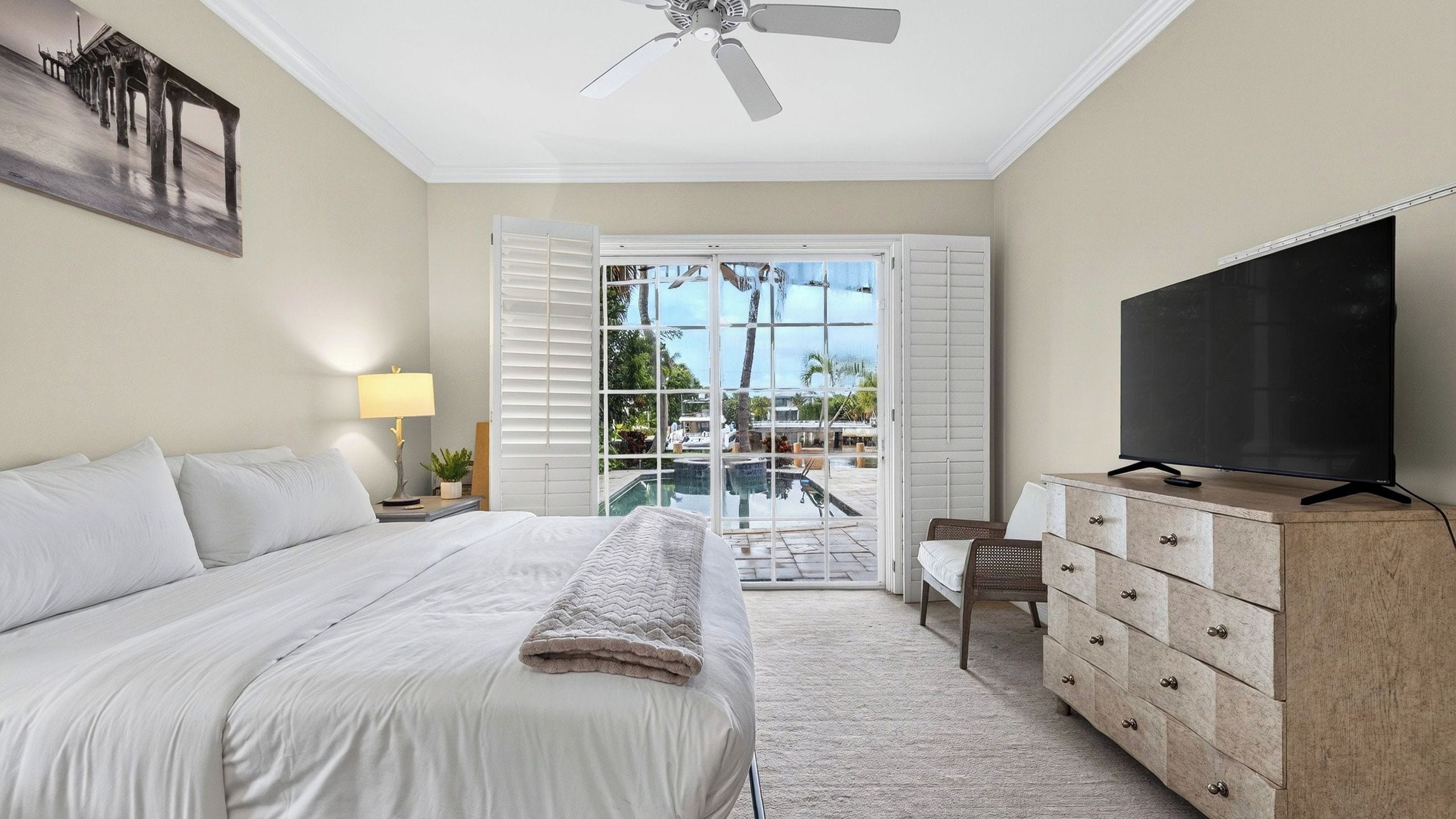 A hotel room with a bed, a television, a dresser, and a view of the outdoors through a sliding glass door.