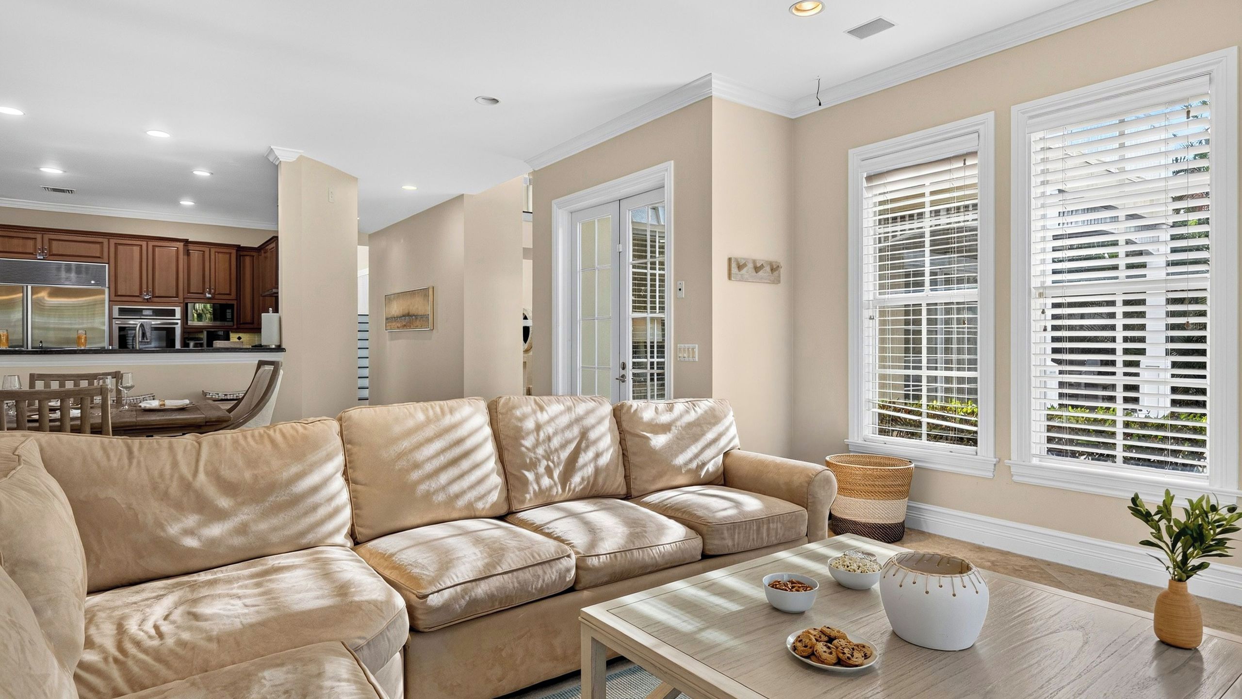A living room with a beige sectional sofa, a dining area with a wooden table and chairs, and a kitchen with modern appliances.