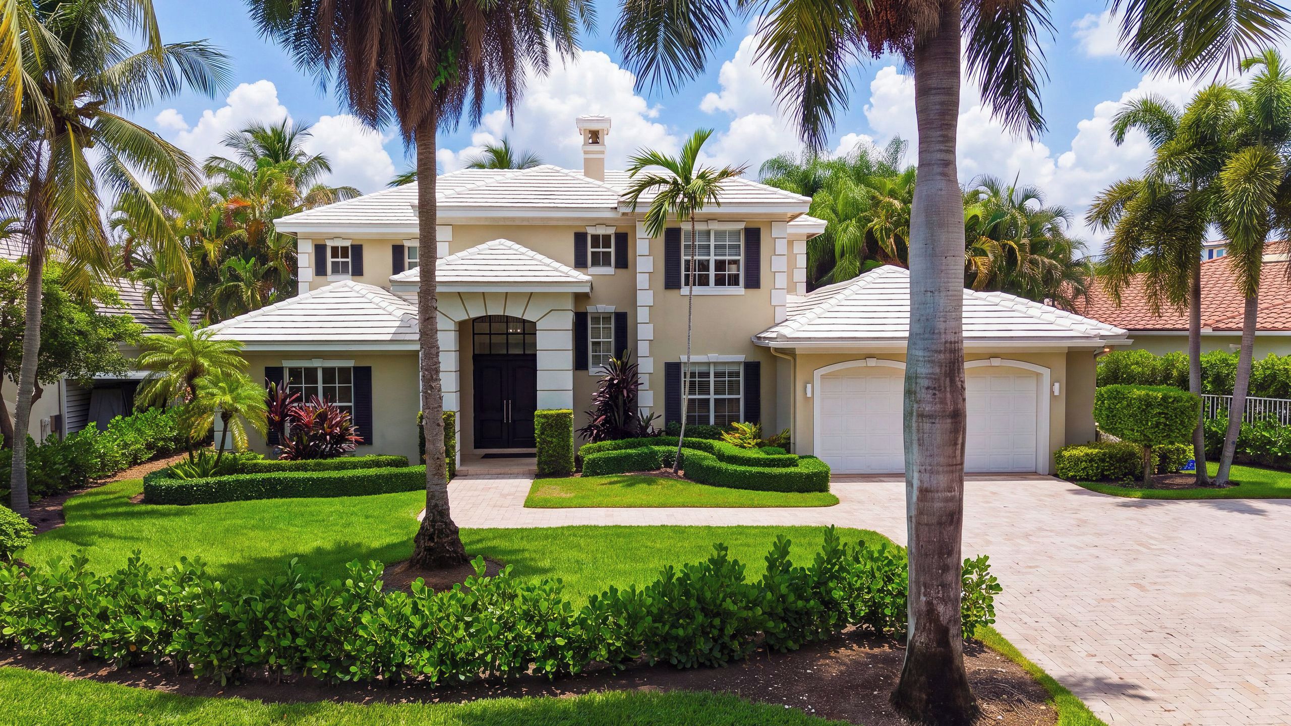 A two-story house with a well-maintained lawn, palm trees, and a garage.