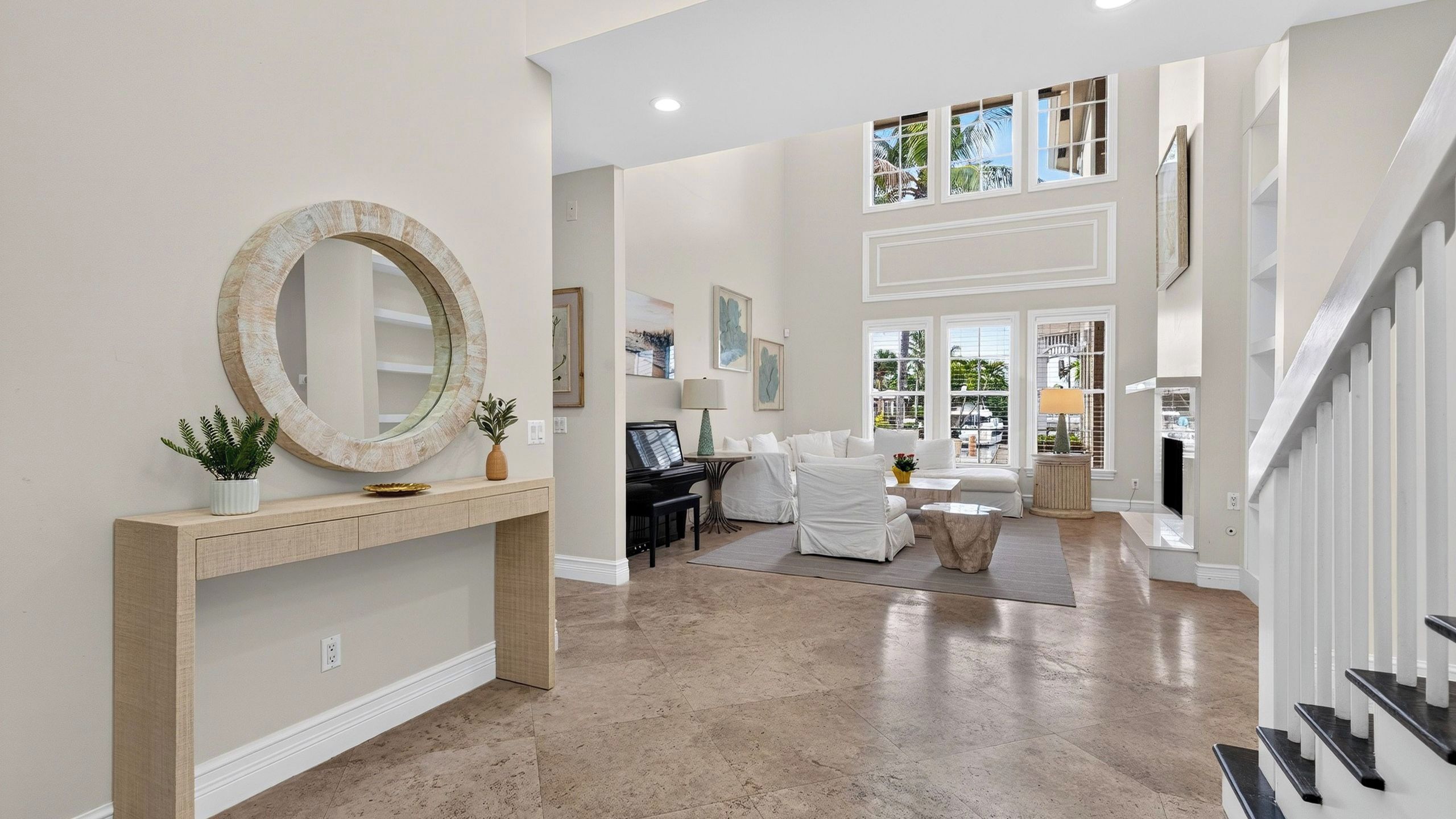 A spacious living area with a piano, white furniture, and a large mirror on a console table.