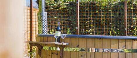 A wooden outdoor seating area with a bottle of wine and two glasses on a table.