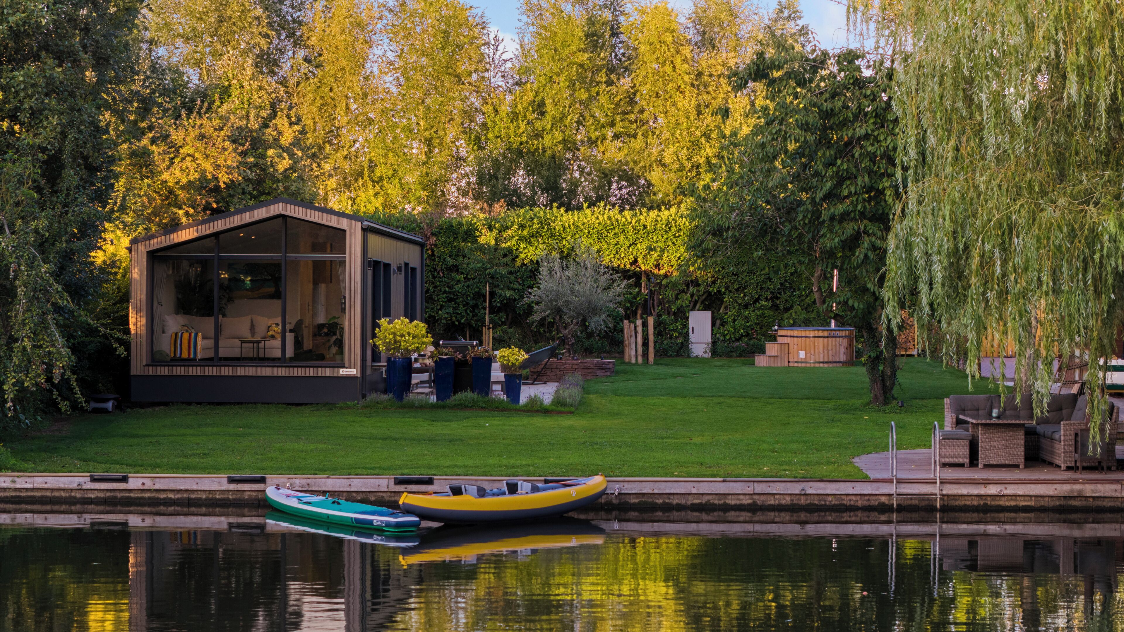 A serene lakeside property with a wooden cabin, a hot tub, and a boat docked by the water.