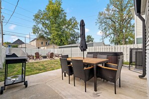 An outdoor patio with a table and chairs, a grill, and a covered seating area. - Hot Tub + Fire Pit Yard · Near Fountain Square (Indianapolis)