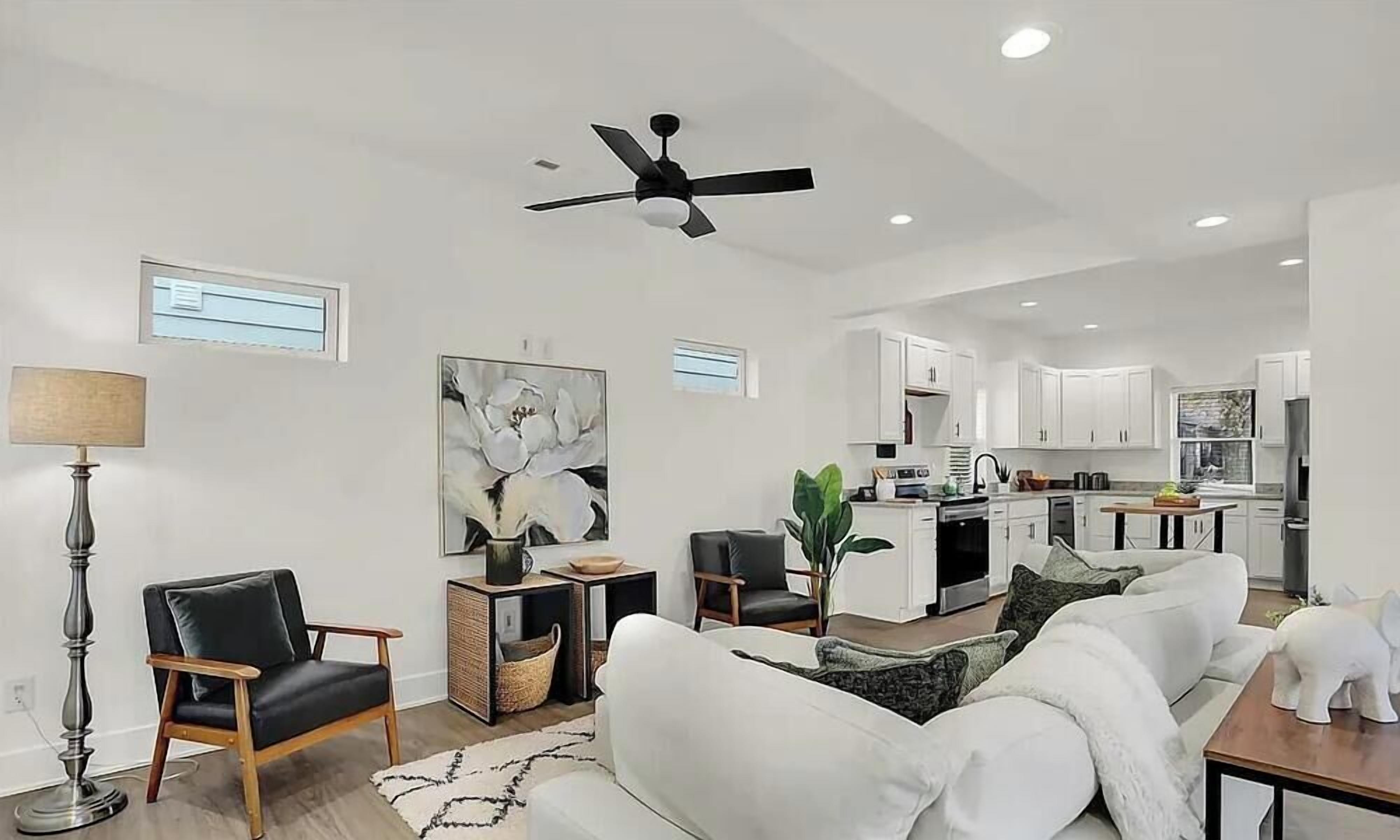 A modern living room with a sofa, a coffee table, and a floor lamp. There is a kitchen area with cabinets and a dining table.