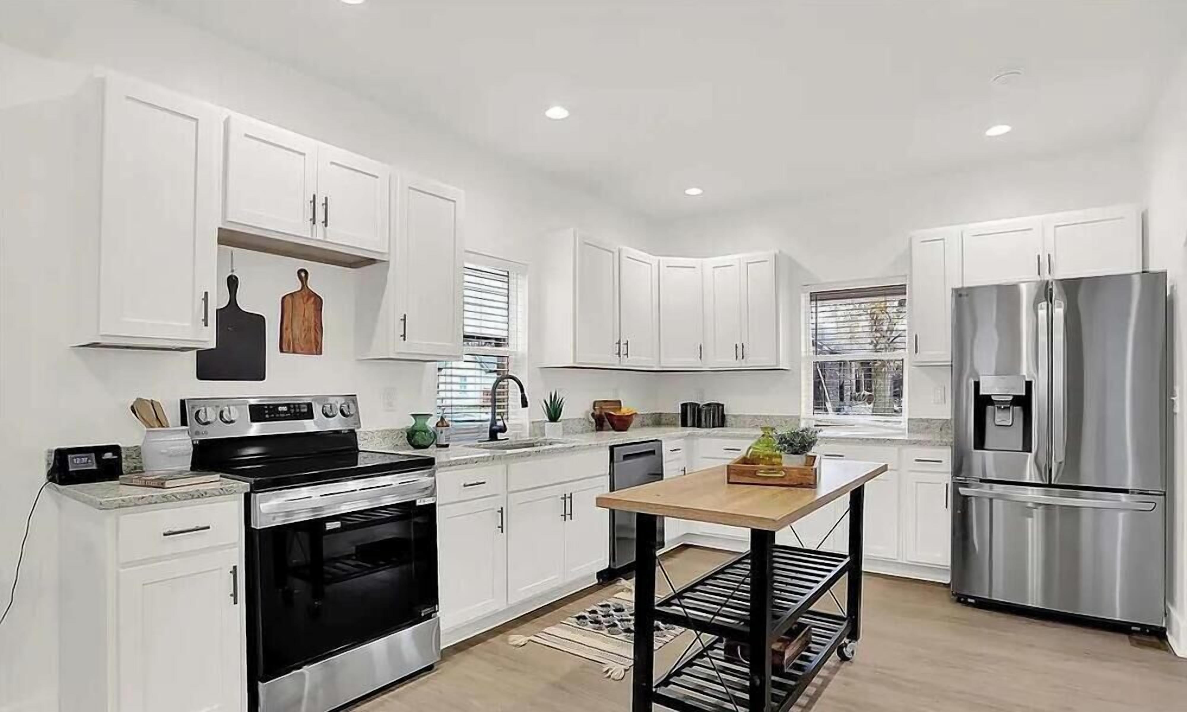 A modern kitchen with white cabinets, stainless steel appliances, and a wooden dining table.