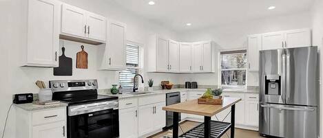 A modern kitchen with white cabinets, stainless steel appliances, and a wooden dining table.