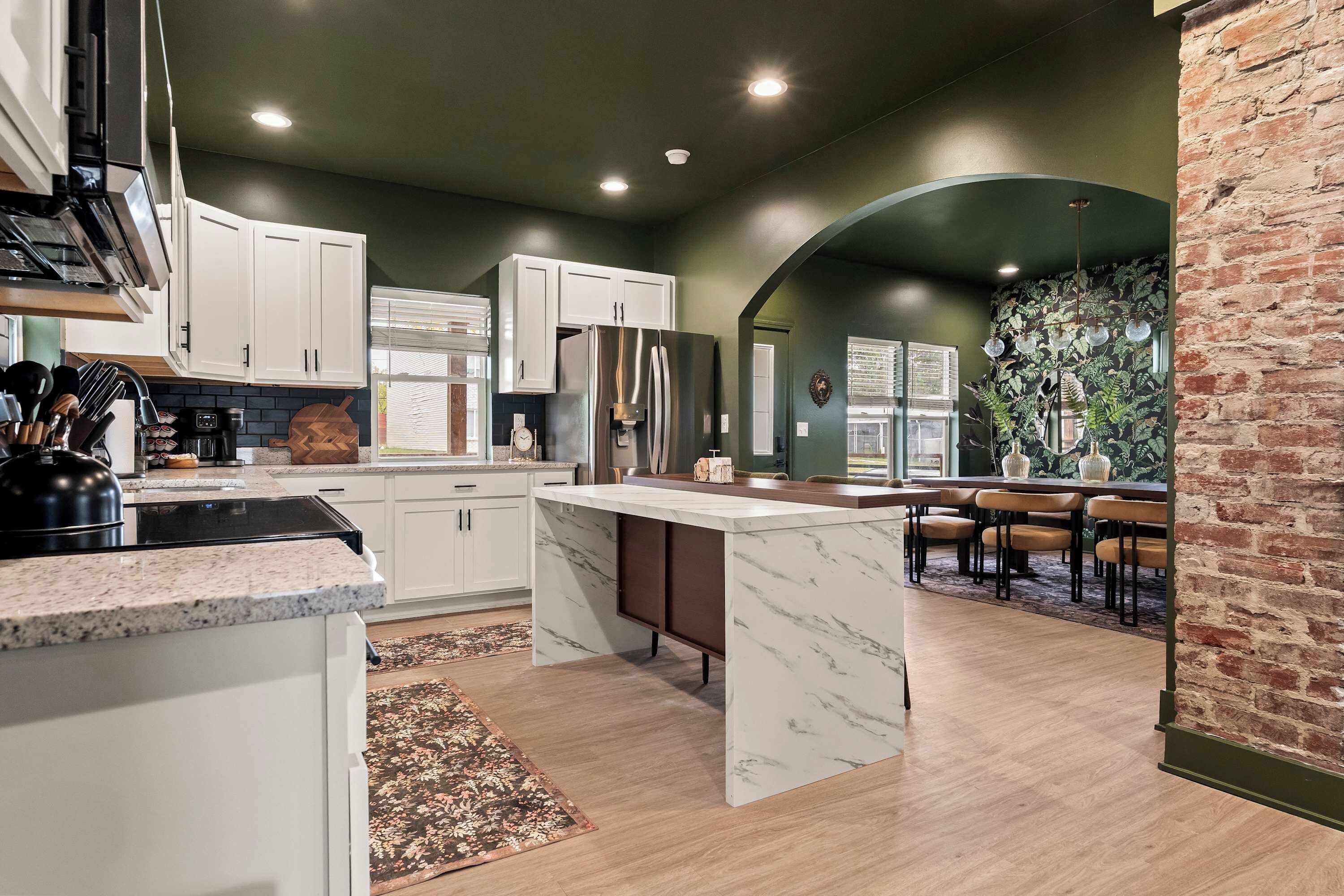 A modern kitchen with white cabinets, a marble island, and a brick accent wall.