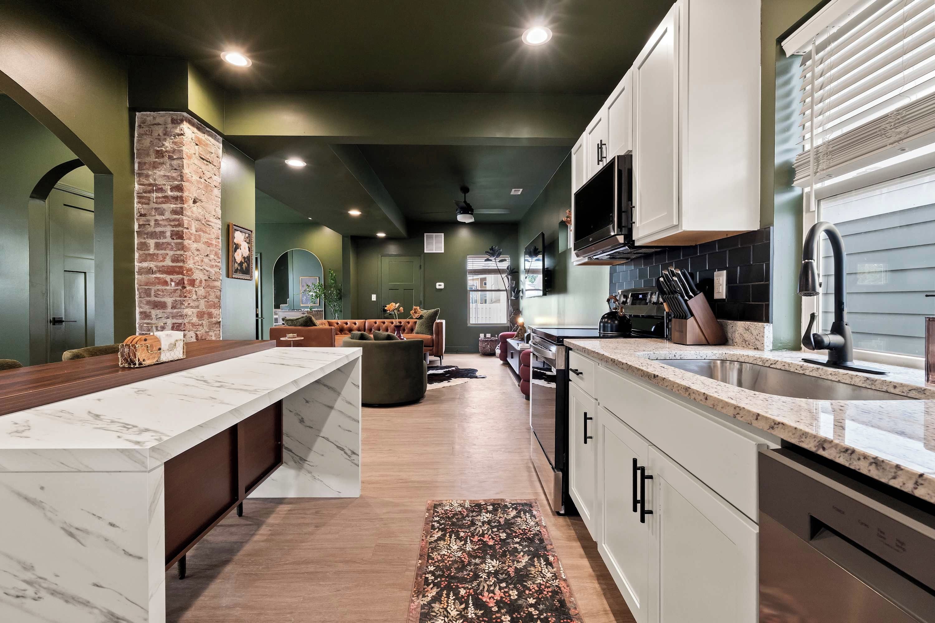 A modern kitchen with a marble countertop, a built-in oven, and a large window with blinds.